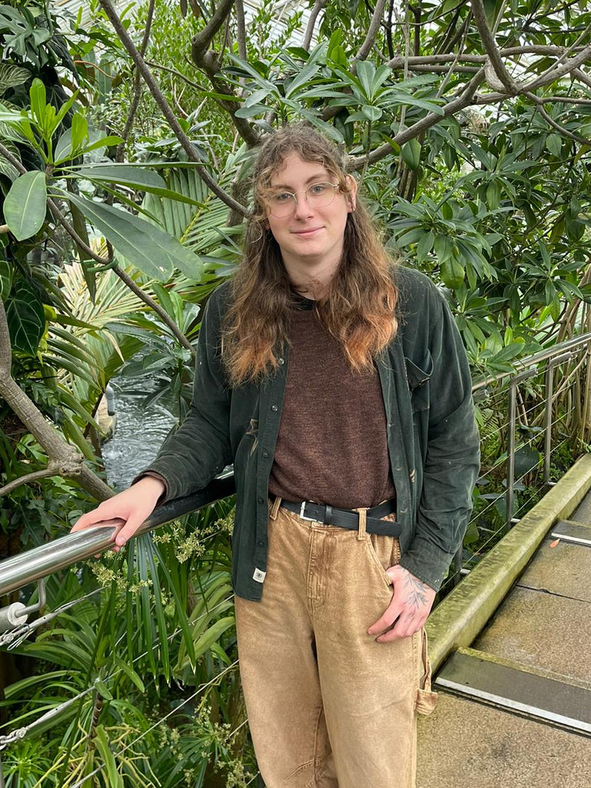 Sam standing in a lush green tropical setting with plants and a pathway.